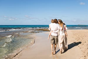 Familie mit zwei Kindern auf den armen der Eltern laufen am Strand.