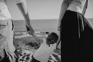 Vater und Mutter halten Kind in der Mitte an der Hand.