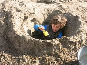 Junge buddelt tiefes Loch am Strand.